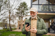 © Miljan Živković - One senior man stand in front of tiny house in day use smart phone