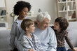 © fizkes - Happy senior grandfather enjoying meeting with diverse little grandkids, hugging, cuddling boys, sitting on sofa. Cheerful grandchildren visiting grandpa at home, hugging granddad, laughing