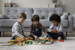 © fizkes - Three diverse little preschool boys playing with toys on heating carpeted floor, enjoying leisure, playtime, developing game, constructing city roads from building blocks together