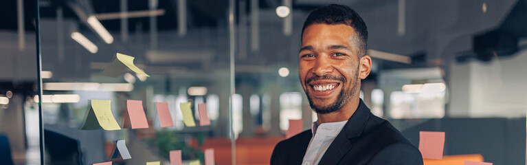 Poster - Portrait of smiling african businessman standing in office with crossing hands