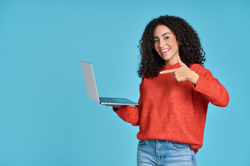 Wall Mural - Young happy latin woman pointing at laptop isolated on blue background. Smiling female model holding computer presenting advertising job search or ecommerce shopping website.