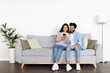© Prostock-studio - Relaxed multicultural couple sitting on sofa, using smartphone