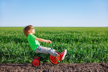 Canvas Print - Happy child riding bike outdoor in spring green field