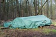 A green waterproof tarpaulin protecting chopped tree logs from bad weather in the forest