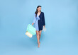 beautiful smiling Asian shopaholic woman holding shopping bags walking to shop summer sale on blue studio background.