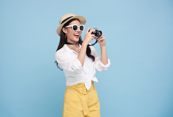 Wall Mural - Happy smiling young asian woman tourist in summer hat standing with camera taking photo isolated on blue studio background