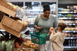 © Seventyfour - Portrait of real black woman shopping in supermarket with little daughter and buying fresh vegetables