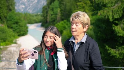 Sticker - A young girl taking a selfie with her grandmother along a mountain river