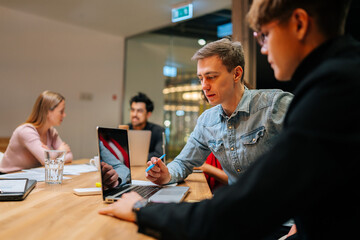 Closeup of young startup business team discussing online project working together on laptop computer at business meeting on modern boardroom. Caucasian male and female colleague working on background.