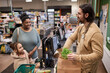 Side view portrait of smiling male worker in supermarket helping young woman with groceries