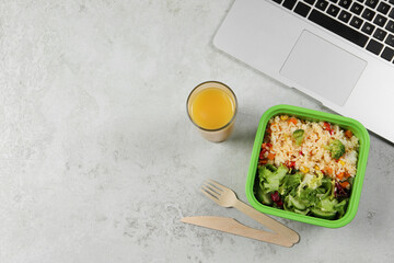 Wall Mural - Container of tasty food, laptop, cutlery and glass of juice on light grey table, flat lay with space for text. Business lunch