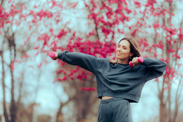 Pretty Woman Working out with pink Dumbbells in the Park. Cool relaxed lady training outdoors using weights 
