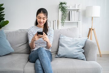 Wall Mural - Asian beautiful woman sitting on sofa and swipe mobile phone in house. 