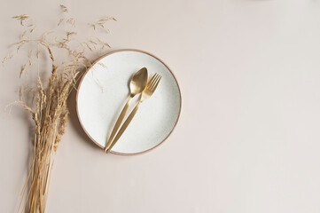 Wall Mural - beige empty plate with golden cutlery on beige background with dried flowers bouquet. Boho minimalist aesthetic. Dishware mock up