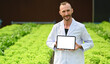 © Prathankarnpap - Portrait of agricultural researcher showing digital tablet standing in greenhouse. Blank screen for advertising text message