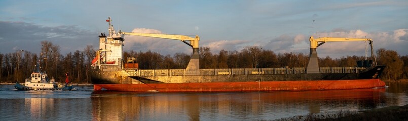 Canvas Print - Cargo ship entering port assisted by tugboat