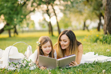 Happy family mom and daughter are watching an album with photos in the summer in the park or in the garden