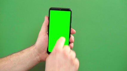 Mobile phone in young man hand. Use smartphone with blank green screen on green color studio background. Male showing black phone with chroma key display. Close up. Mock up of smart phone for Ad, app