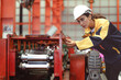 © Nassorn - Latin woman engineer inspecting heavy machinery system in production line for manufacturing safety. Female technician doing repair service. Maintenance machine equipment in metalwork factory concept.