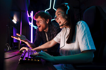 Asian girl winning in video game while her friend assisting her in cybersport club