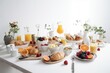  a white table topped with plates of food and cups of orange juice and juicer next to a bowl of fruit and a pitcher of orange juice.  generative ai