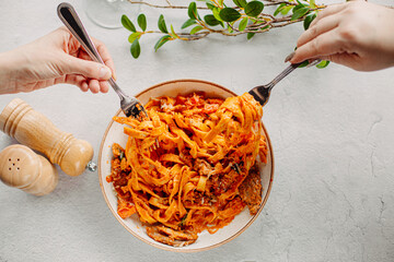 Italian pasta, tomato sauce. Two female hands in the frame, girls eat pasta, hold forks in their hands, top view, Italian cuisine.