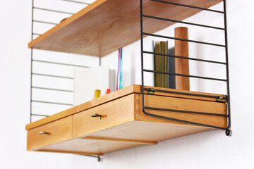 a mid century String Shelf with drawers original from the 60s mounted on a white wall with books and other accessories with a commode made of teak wood scandinavian design orange chair living room 60s