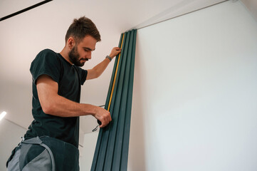 Wall Mural - Taking measurements. Plumber worker installing heating radiator in empty room of a newly built house