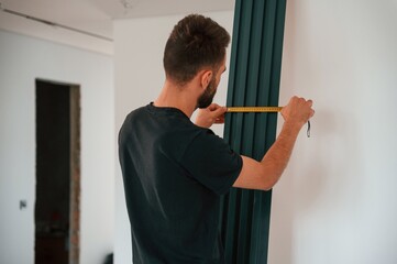 Wall Mural - Taking measurements. Plumber worker installing heating radiator in empty room of a newly built house