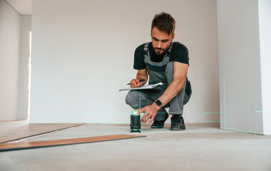 Wall Mural - Laser leveler device. Man is installing new laminated wooden floor