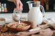 Aesthetic breakfast. Milk jug pouring milk into the bowl with natural muesli made from mix of unprocessed whole grains