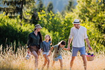 Wall Mural - Happy young parents with daughters walking for picnic in nature in summer day,