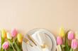 Mother's Day atmosphere concept. Top view photo of circle plate with cutlery knife fork and napkin with gold ring and yellow pink tulips on isolated pastel beige background with copy space