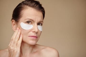 Wall Mural - Mature woman applying undereye patches in the morning to get rid of puffiness