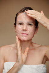 Wall Mural - Mature woman applying sheet mask of her face after morning shower