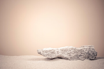 Grungy stone platform podium for cosmetics or products presentation on white beach sand and beige color background. Front view