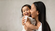 © Prostock-studio - Joyful Asian Mom Hugging Baby Daughter Over Gray Wall Indoor