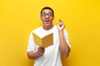© Богдан Маліцький - pensive guy african american student in white t-shirt and glasses writes in notebook and plans on yellow background