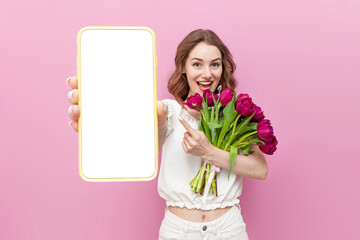 young attractive girl in white clothes holds bouquet of pink tulips and shows blank screen of smartphone