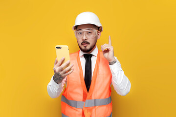 Wall Mural - asian foreman in uniform holding smartphone and pointing idea with his finger on yellow isolated background