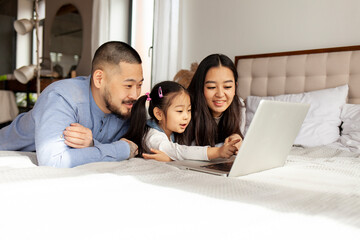 Wall Mural - asian family use laptop at home on bed, korean dad mom and little daughter look at computer screen and study online