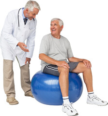 Male therapist looking at senior man sit on exercise ball