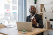 © sofiko14 - African male entrepreneur dressed in formal wear having video conference at modern office. Self-assured man leading online meeting with help of wireless headset and laptop.