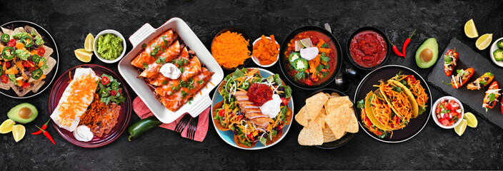 Wall Mural - Mexican food table scene. Top down view on a dark stone banner background. Tacos, burrito plate, nachos, enchiladas, tortilla soup and salad.