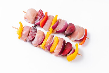 Wall Mural - Skewers with pieces of raw meat, red, yellow and green pepper.Top view.Raw chicken leg meat skewers with vegetables,plums,peppers,onions, on a white background.Uncooked mixed meat skewer with peppers.