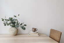 Silver Green Eucalyptus Tree Branches In Beige Textured Vase. Brown Cup Of Coffee, Tea And Old Books On Wooden Table. White Wall Background. Minimalistic Scandinavian Interior, Dinning Room. Breakfast