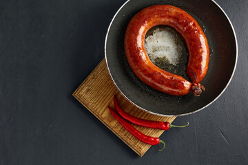 Wall Mural - Grilled pork sausage ring in a cast iron pan and hot peppers on a cutting wooden board on a dark stone table