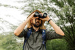 Hiker with backpack using binoculars in the wild. Field biologist or naturalist using binoculars to study wildlife or nature.
