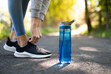 Drinking water and staying hydrated. Person running in the park trying shoe next to bottle of water. 