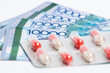 © Roman - Blister with pills drug on top of stack of Tenge Kazakhstan money bills on white background.
